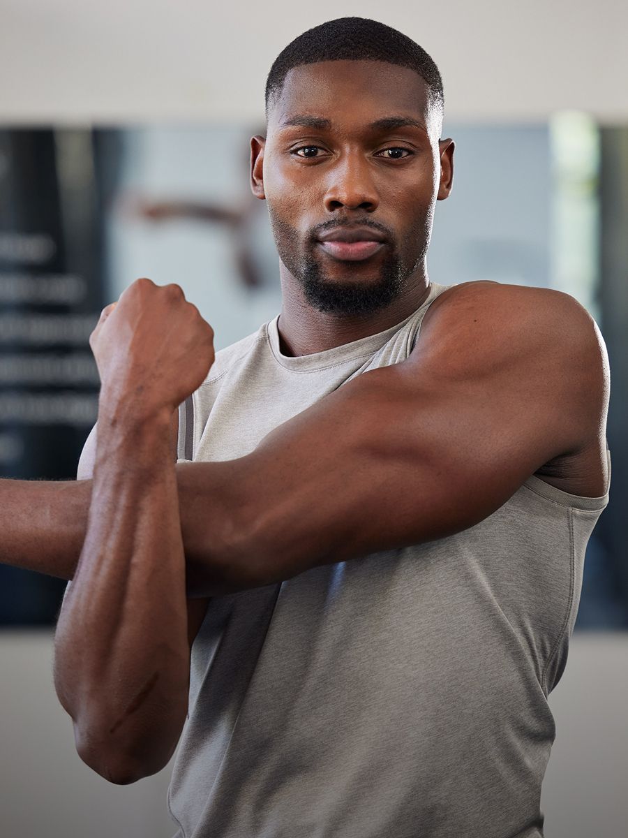 Man stretching arm in gym outfit indoors.