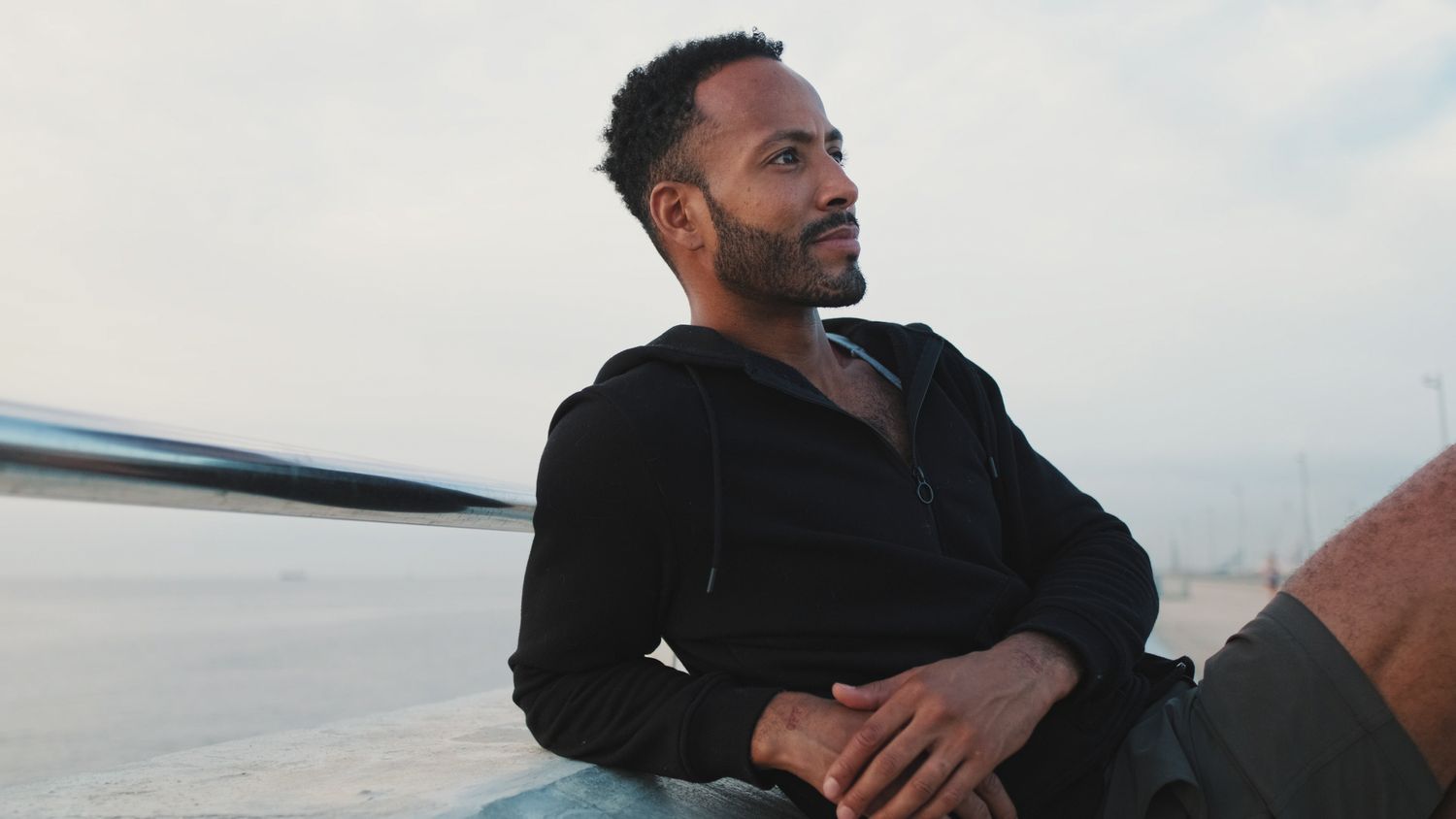 Man relaxing by the shore, wearing a hoodie.