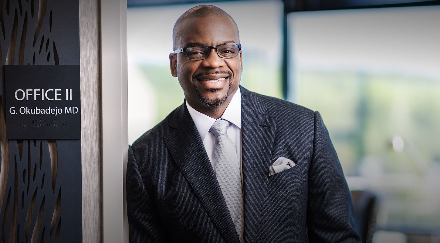 Doctor standing by office entrance, smiling confidently.